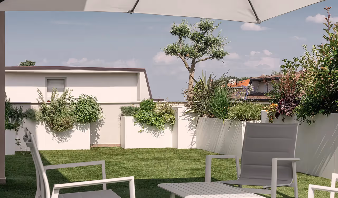 Giardino su terrazza con prato verde, poltrone da esterno grigie sotto un ombrellone e fioriere modulari bianche ad angolo piene di piante e piccoli alberi.