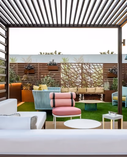 Area lounge outdoor con pergola moderna, pannelli frangivista decorativi tagliati al laser e fioriere Modularte integrate in un giardino pensile.