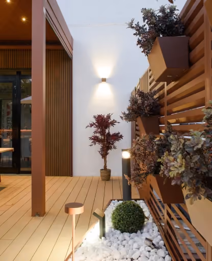 Parete verde attrezzata Modularte con pannelli frangivista in metallo, fioriere sospese coordinate e illuminazione outdoor integrata su deck in legno.