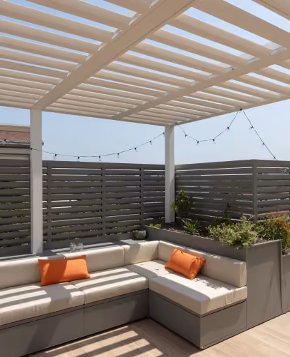 Pergola moderna con lamelle orientabili, pannelli frangivista grigi e divano da esterno integrato in fioriere modulari Modularte.