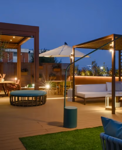 Progetto illuminazione outdoor Modularte con fioriere retroilluminate su terrazzo moderno con pavimentazione in legno e zona lounge serale.